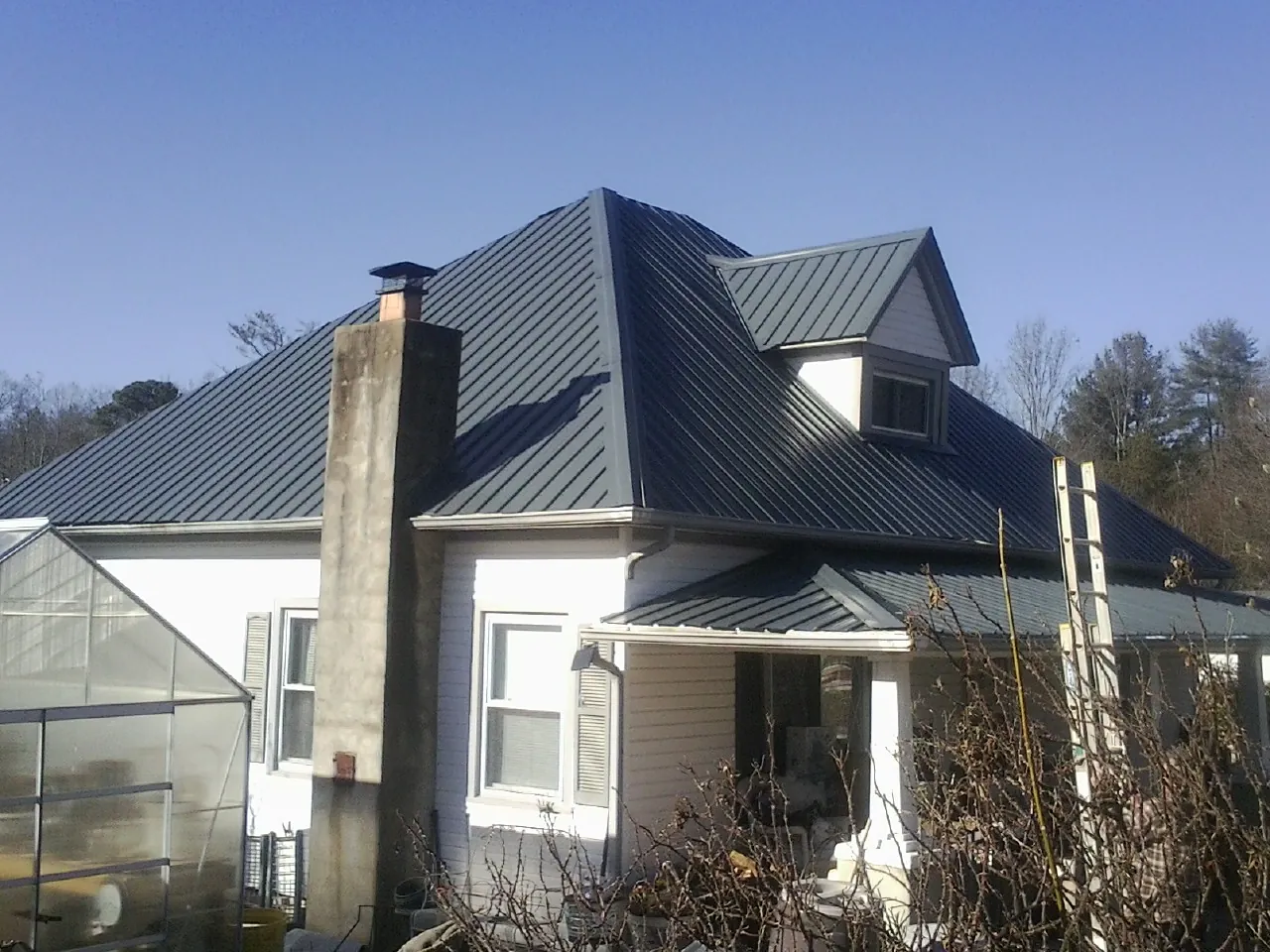 Dark blue standing seam metal roof on a white farmhouse with dormer — Slate & Tile Roof Repair by Roofing Brothers in Center Moriches