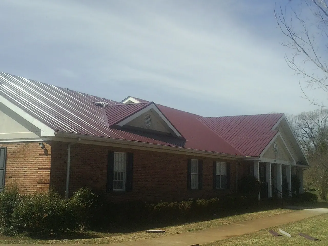 Red metal roof with gabled entries on a long brick building, from a Hail Damage Roof Repair job in Center Moriches