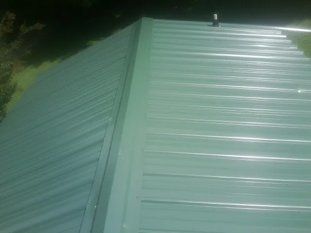 New green metal panels meeting at the ridge of a roof — Flat Roof Repair work by our crew in Center Moriches