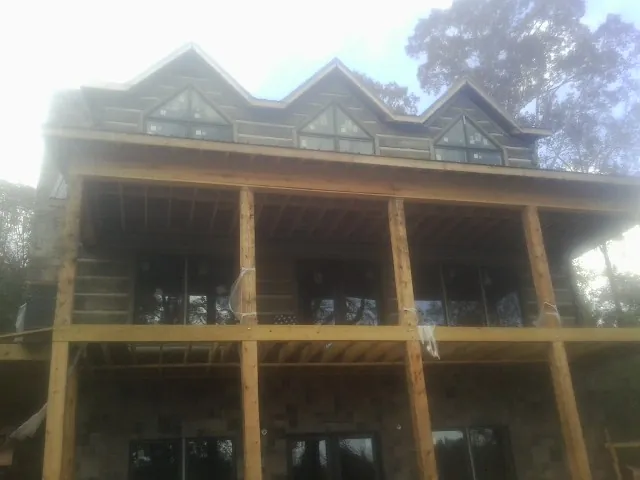 Dormers and porch framing on a large log home under construction — Roof Coating work by our crew in Center Moriches