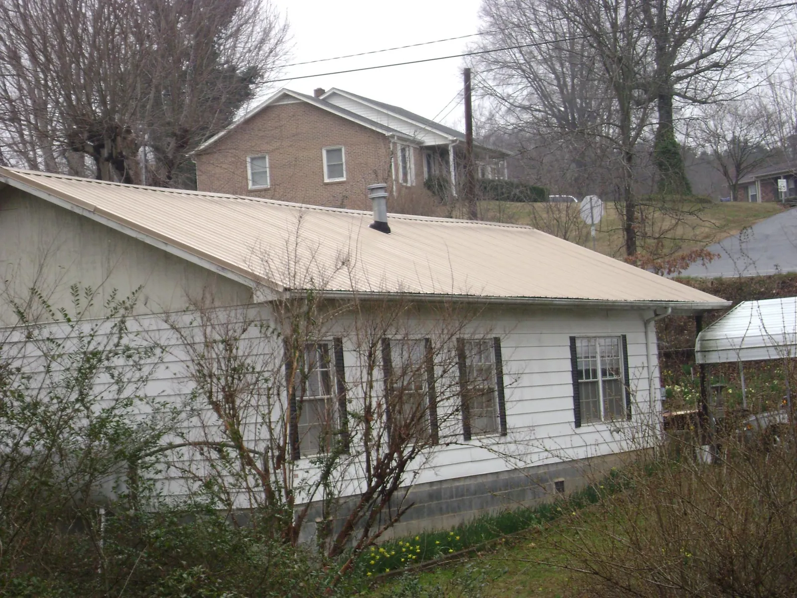 Tan metal roof on a white sided house set into a hillside — Commercial Roofing by Roofing Brothers in Center Moriches