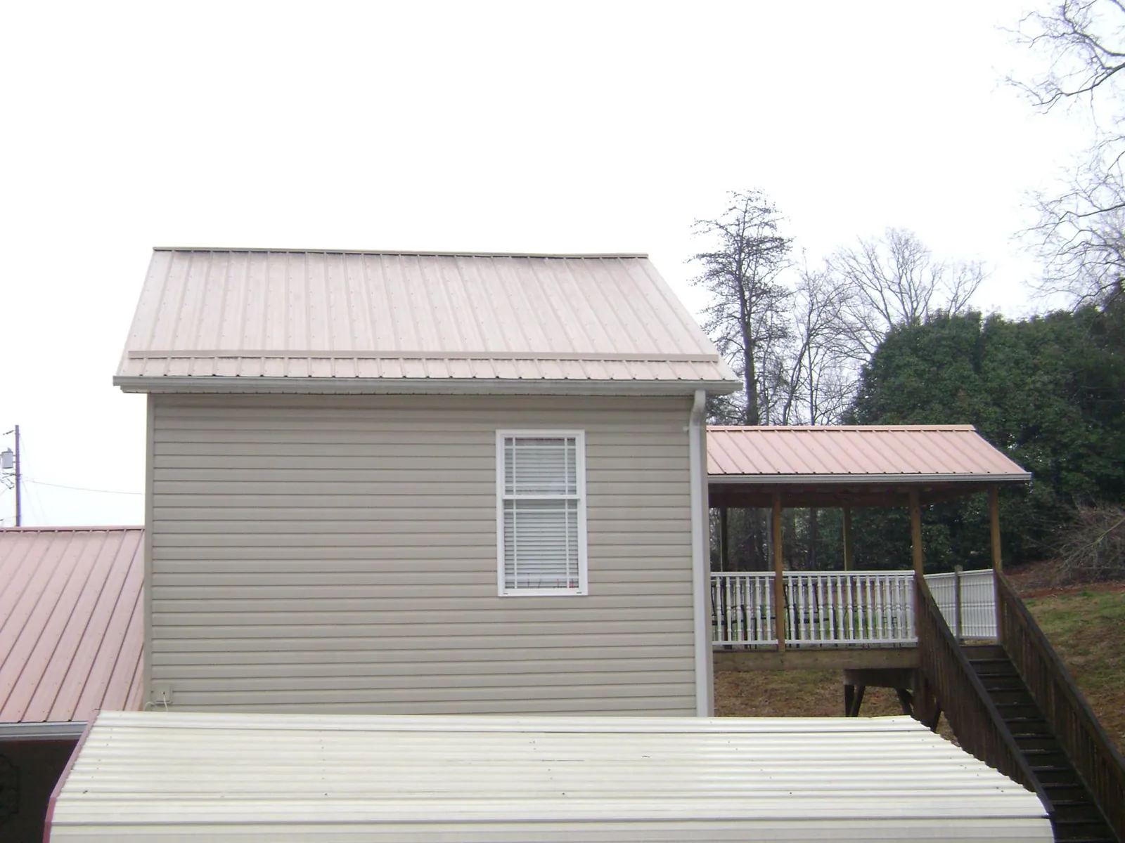 Tan metal roofs on a two story addition and attached porch, from a Roof Replacement job in Center Moriches